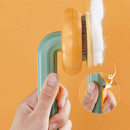 A hand holds a green and orange pet grooming brush against an orange background, with white fur shown coming out of the brush. A circular inset shows a close-up of the handle.