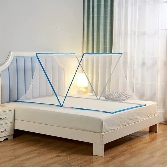 A white wooden bed frame with a padded headboard in a bedroom setting, featuring a blue-framed mosquito net set up over the mattress. The room includes a nightstand, wooden floor, and sheer curtains.