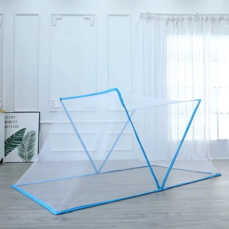 A portable folding mosquito net tent with bright blue frame poles and white mesh, set up on a light gray wooden floor in a bright room with white paneled walls and sheer curtains.