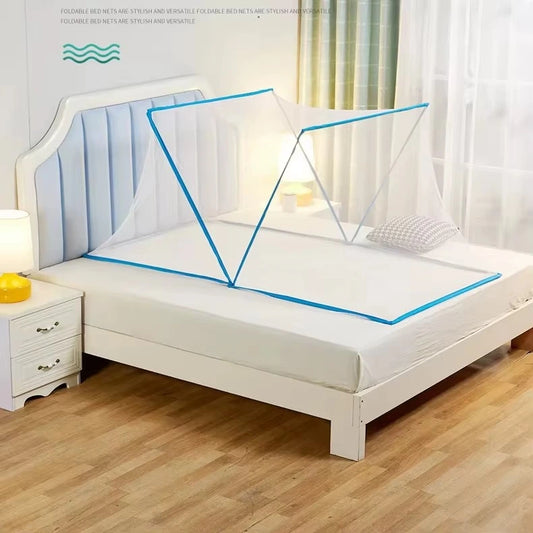 A white bed frame with a padded headboard in a bright bedroom, shown with a blue-edged mosquito net canopy stretched over the mattress. A white nightstand with a lit lamp sits beside the bed, and light wood flooring is visible.